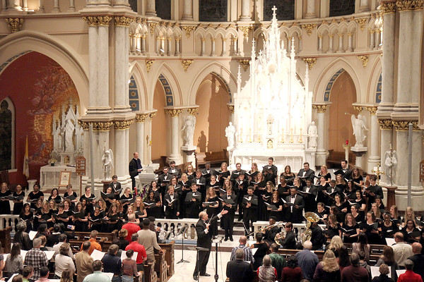 A choir performance inside a cathedral. A large audience is watching as the conductor leads the choir.