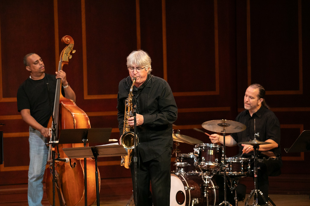 Three musicians perform the bass, saxophone and drums on stage.
