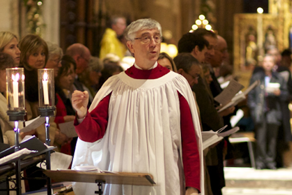 An individual in a white choir robe leads a congregation in song inside a church.
