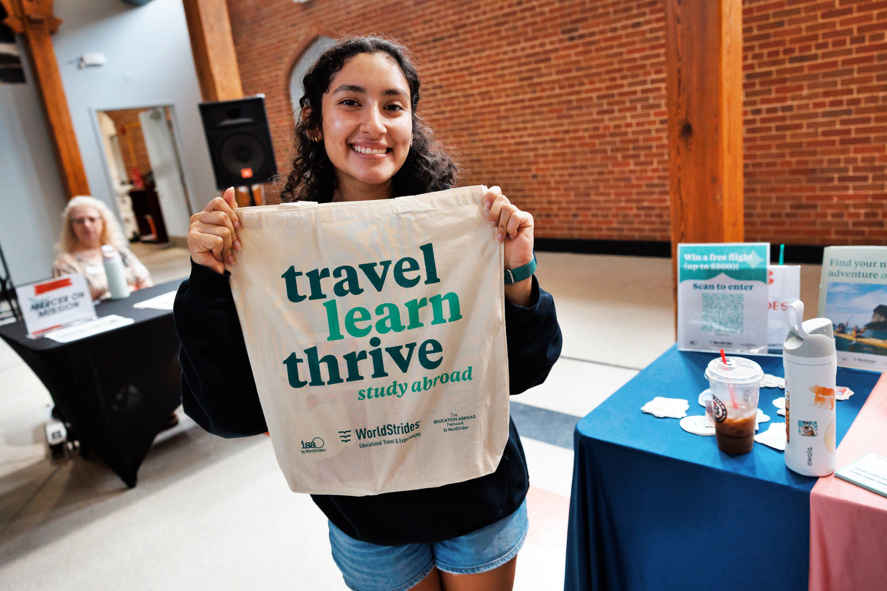 A Mercer student holds up a canvas bag that says Travel, Learn, Thrive on it.