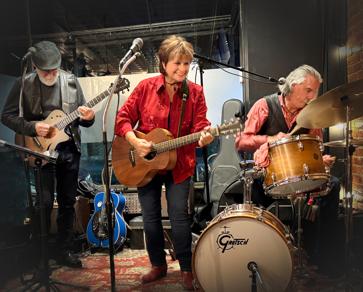 EG Kight performs guitar on stage, alongside another guitarist and a drummer.