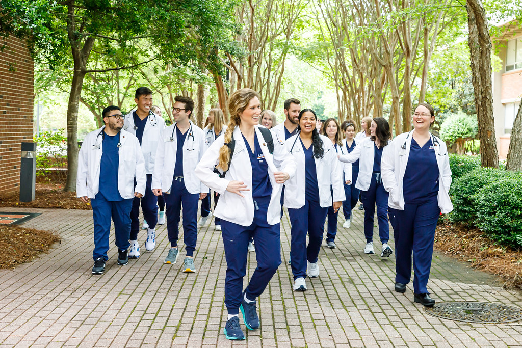 A group of Mercer physician assistant students walking and talking along a tree-lined pathway.