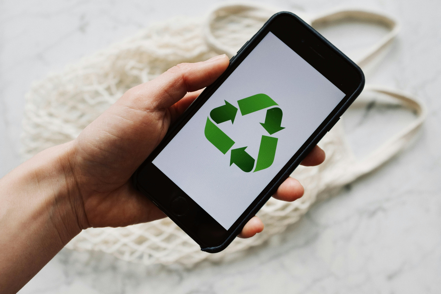 A hand holding an iPhone with a green recycling symbol on it.