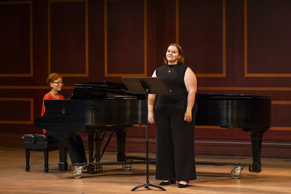 A woman sings on stage alongside a person playing a grand piano.