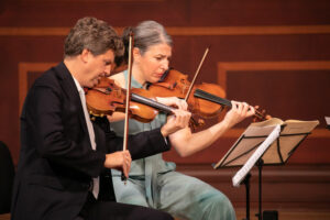 Two violinists perform on stage.