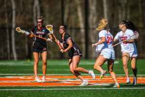 Four women’s lacrosse players compete on a field.