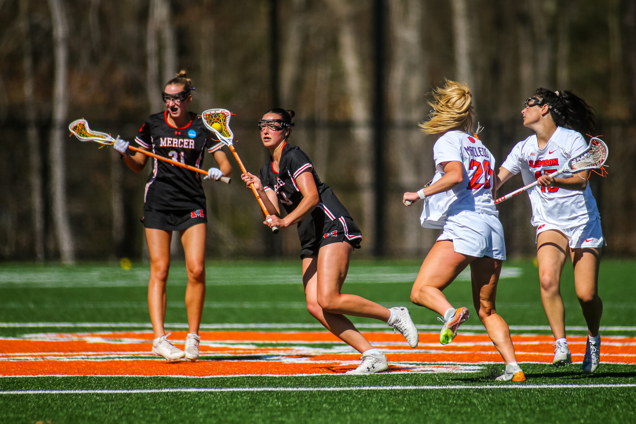 Four women’s lacrosse players compete on a field.