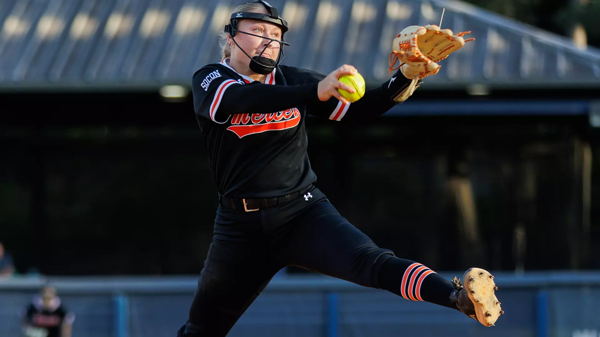 Mercer softball pitcher in mid-pitch, holding a yellow softball, with one leg raised.