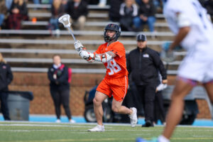 A Mercer lacrosse player prepares to pass the ball during a game on an outdoor field.