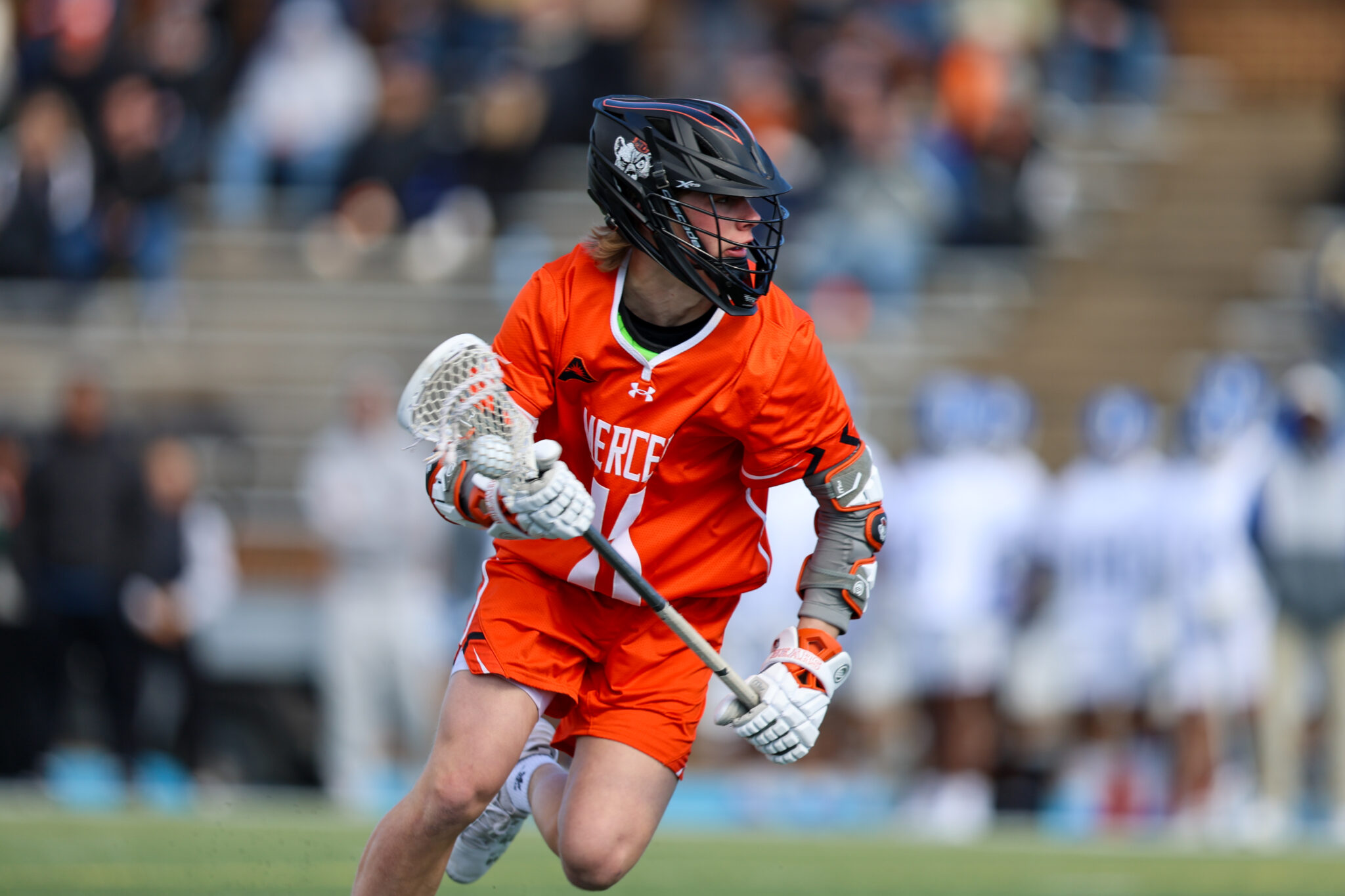 A Mercer lacrosse player runs with the ball during a game on an outdoor field.