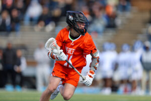 A Mercer lacrosse player runs with the ball during a game on an outdoor field.