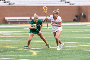 Two female lacrosse players compete for the ball on an outdoor field.