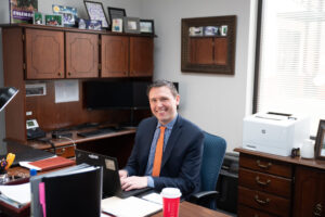 A man sits behind a desk in an office.