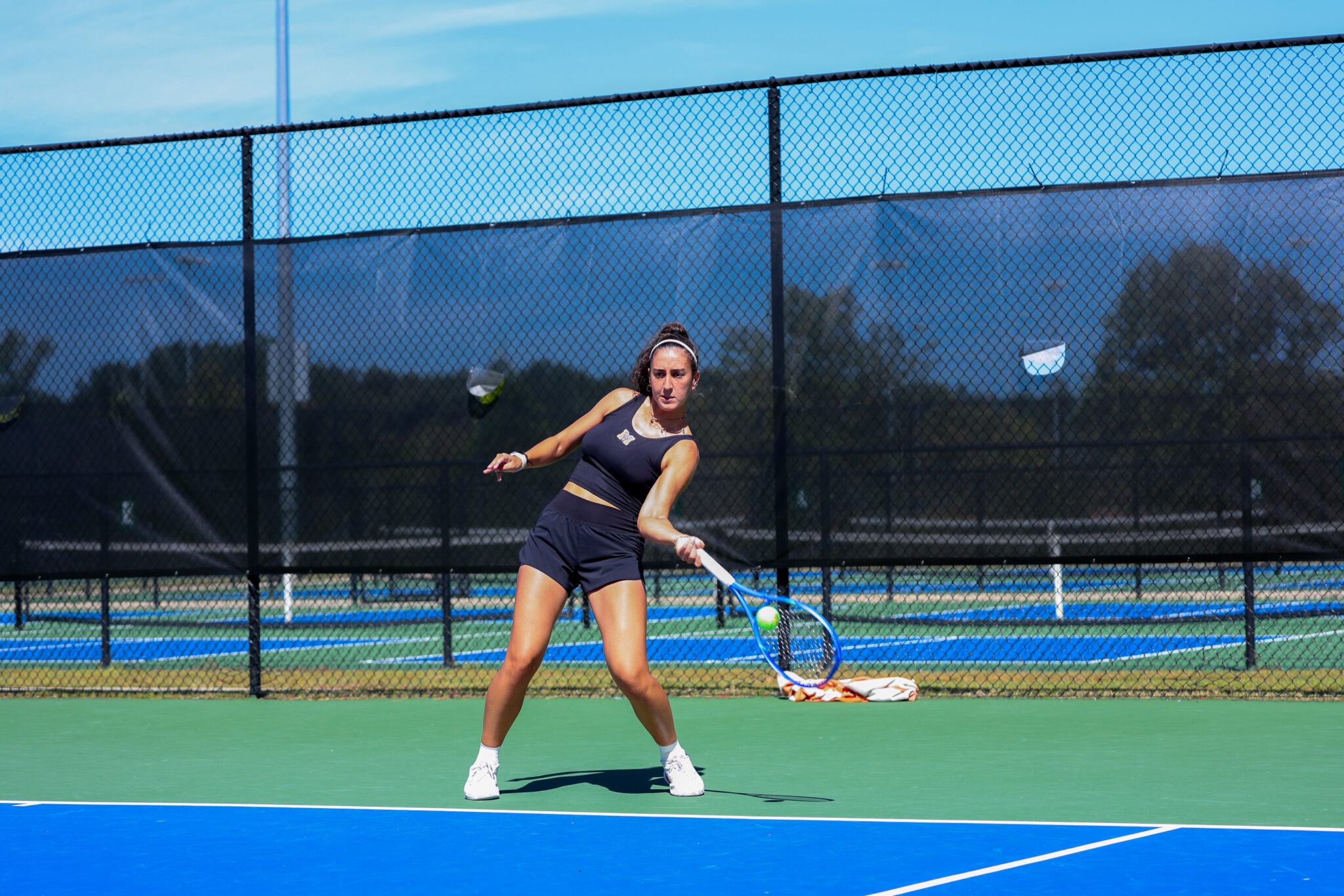 Mercer women's tennis player prepares to hit a forehand shot on an outdoor hard court, with a chain-link fence in the background.