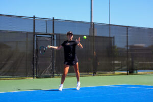 Mercer women's tennis player prepares to hit a tennis ball with a racket on an outdoor court under clear skies.