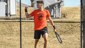 A Mercer men's tennis player stands on a court holding a tennis racket.