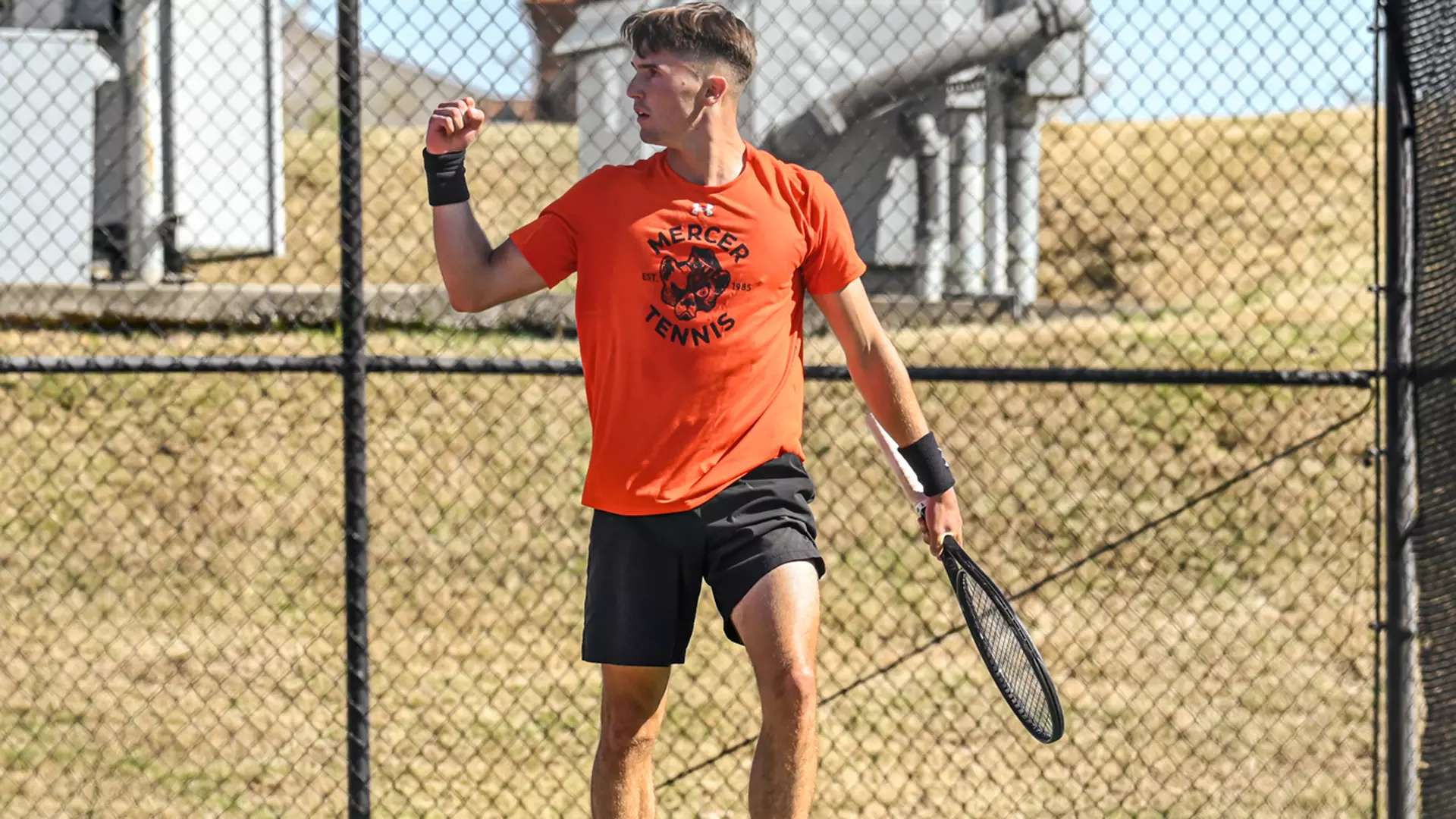 A Mercer men's tennis player stands on a court holding a tennis racket.