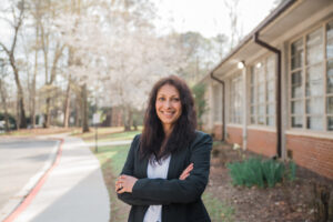 A woman stands outside next to a building.