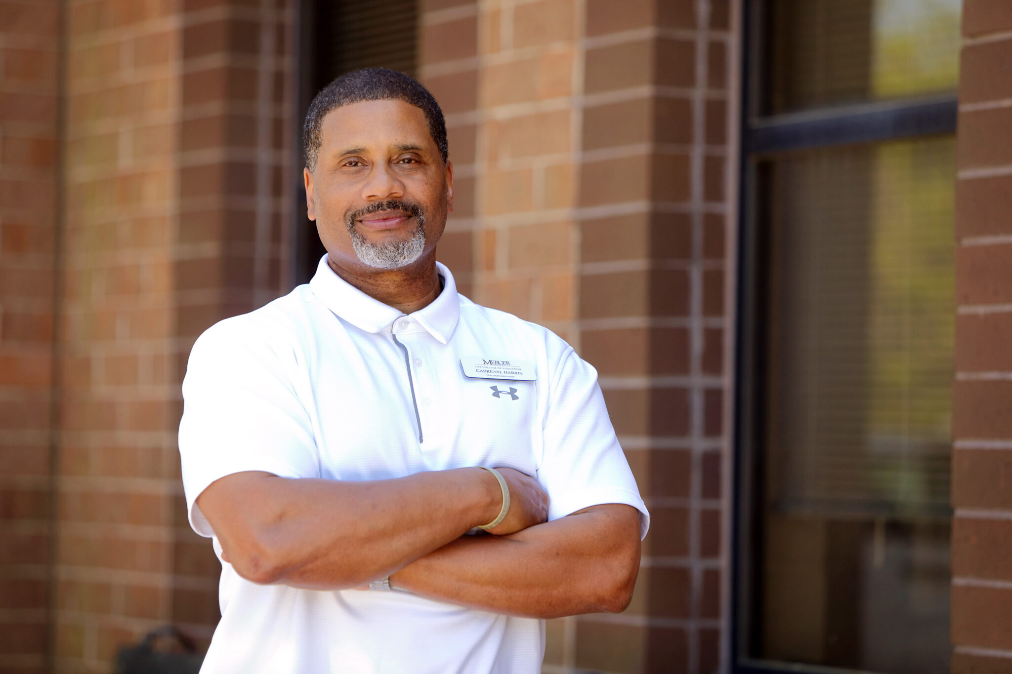 A man stands with arms crossed in front of a brick building.