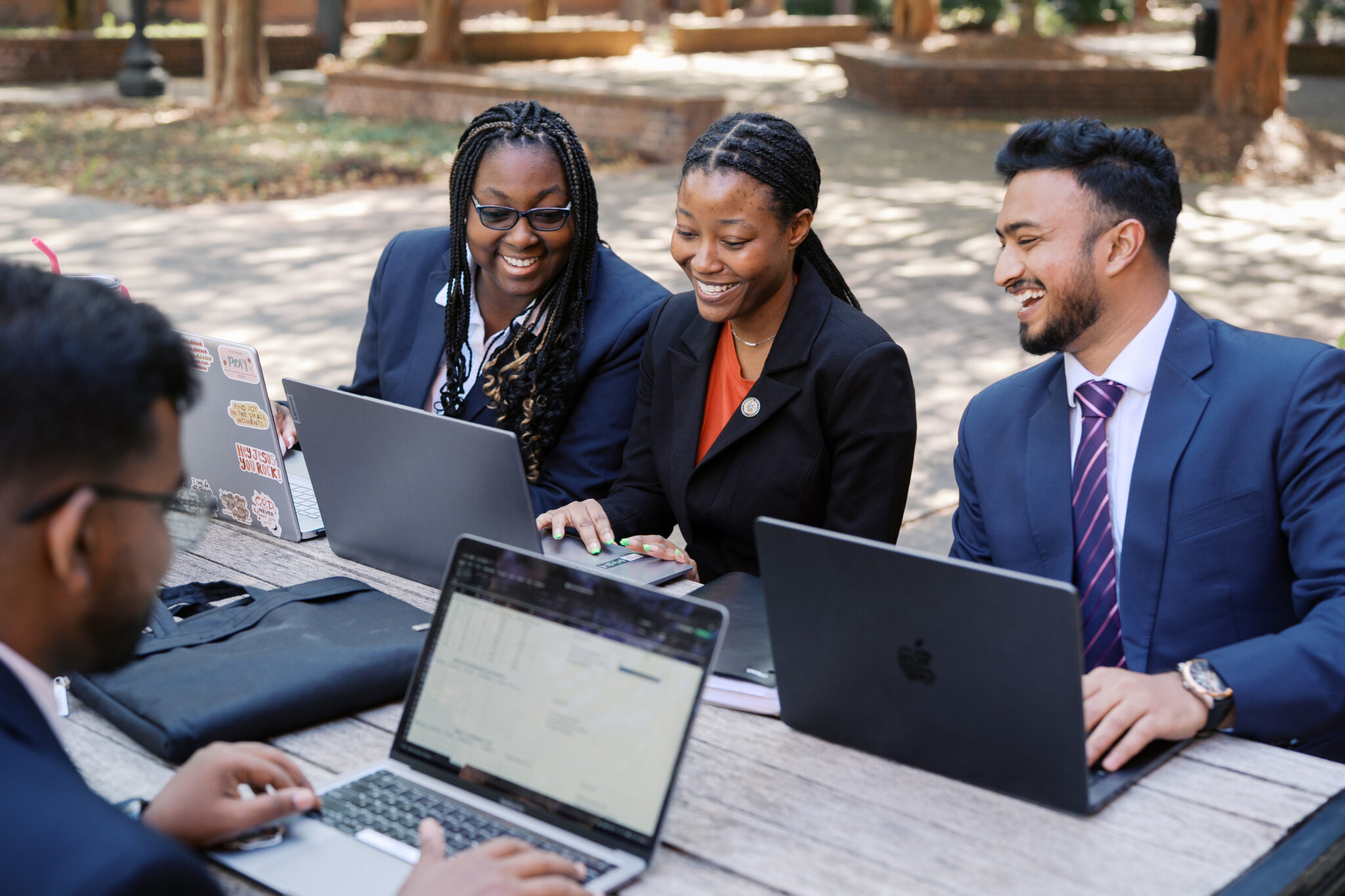 Four Mercer students in business attire work on laptops at a table outside.