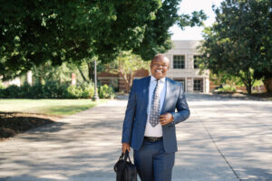 A person wearing a business suit and carrying a briefcase walks on Mercer University's campus.