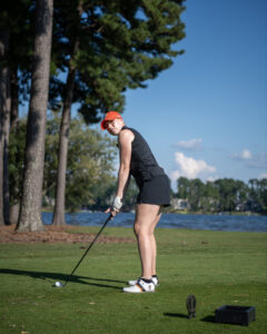 Mercer golfer preparing to swing a club on a golf course near a lake.