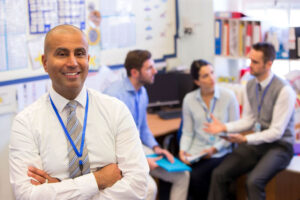 A teacher standing in a classroom with three other teachers in discussion behind him.