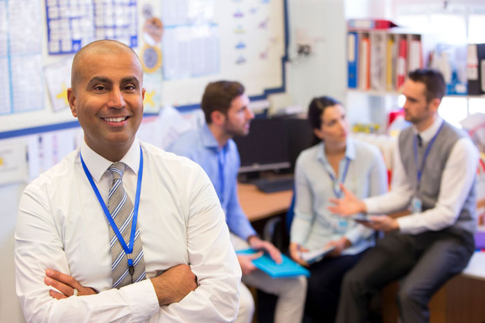A teacher standing in a classroom with three other teachers in discussion behind him.