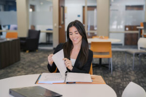 A woman sitting at a round table in an office looks through papers in a binder and smiles.