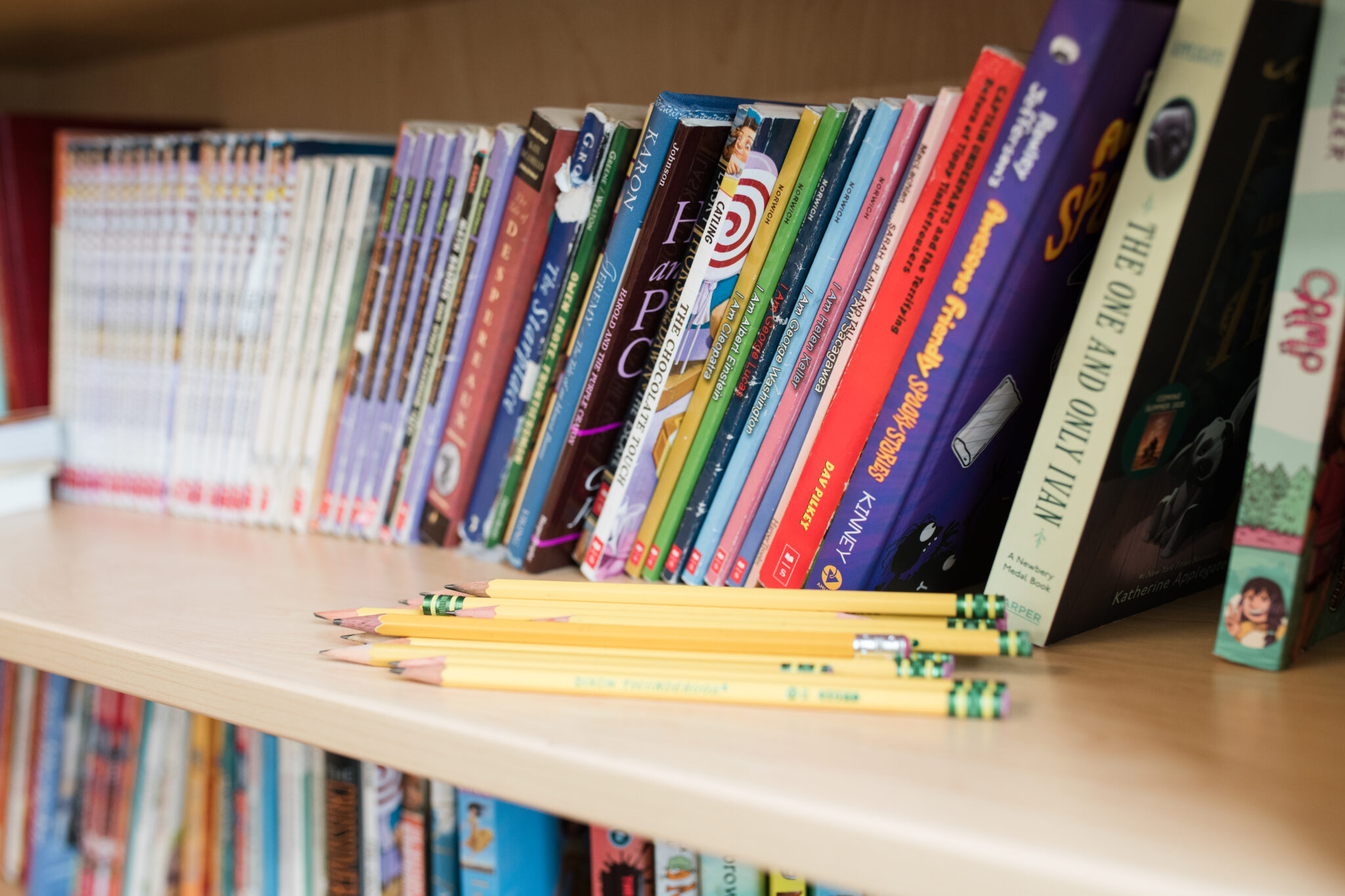 Yellow pencils on a bookshelf with books.