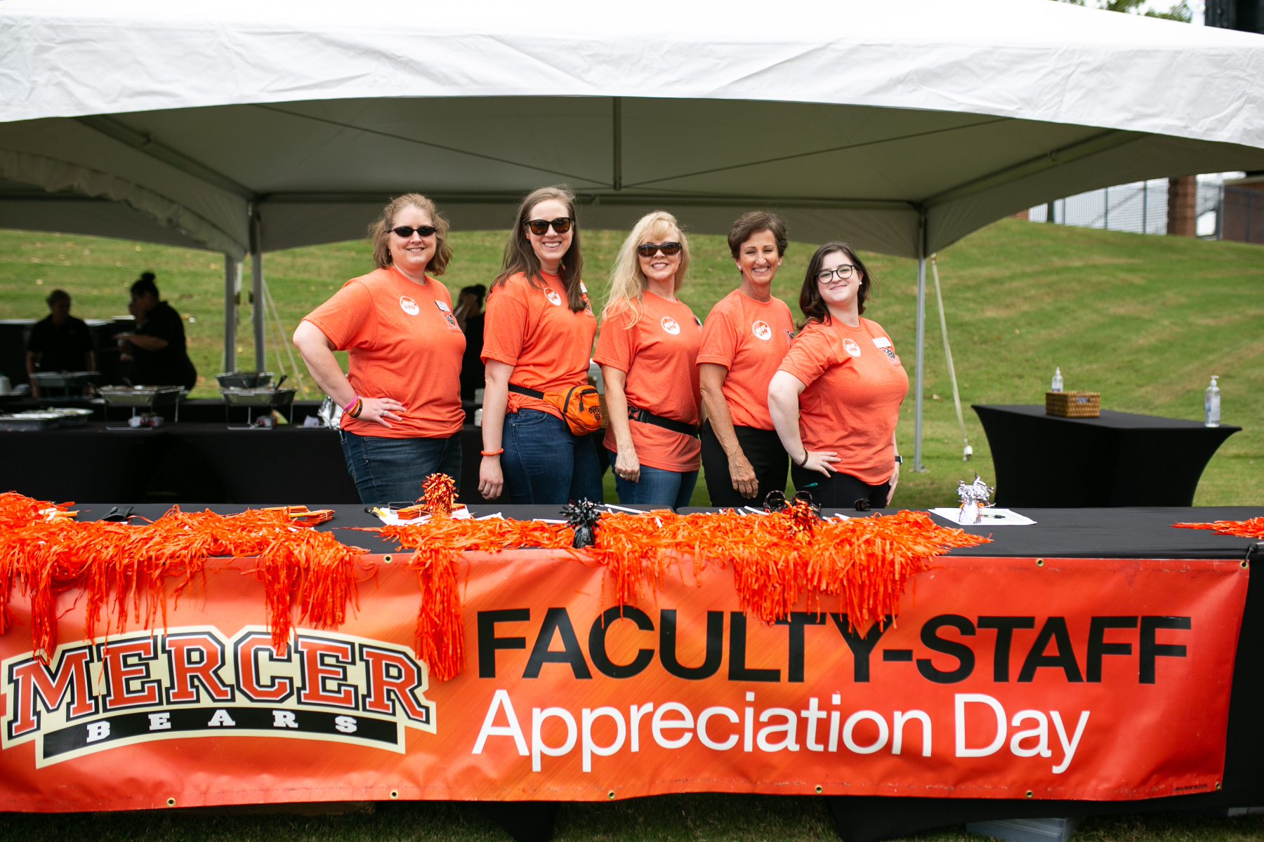 Five people wearing orange shirts stand behind a banner that reads Faculty-Staff Appreciation Day.