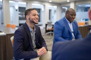 Two Mercer students in business attire sit and talk at a table in a modern office setting.