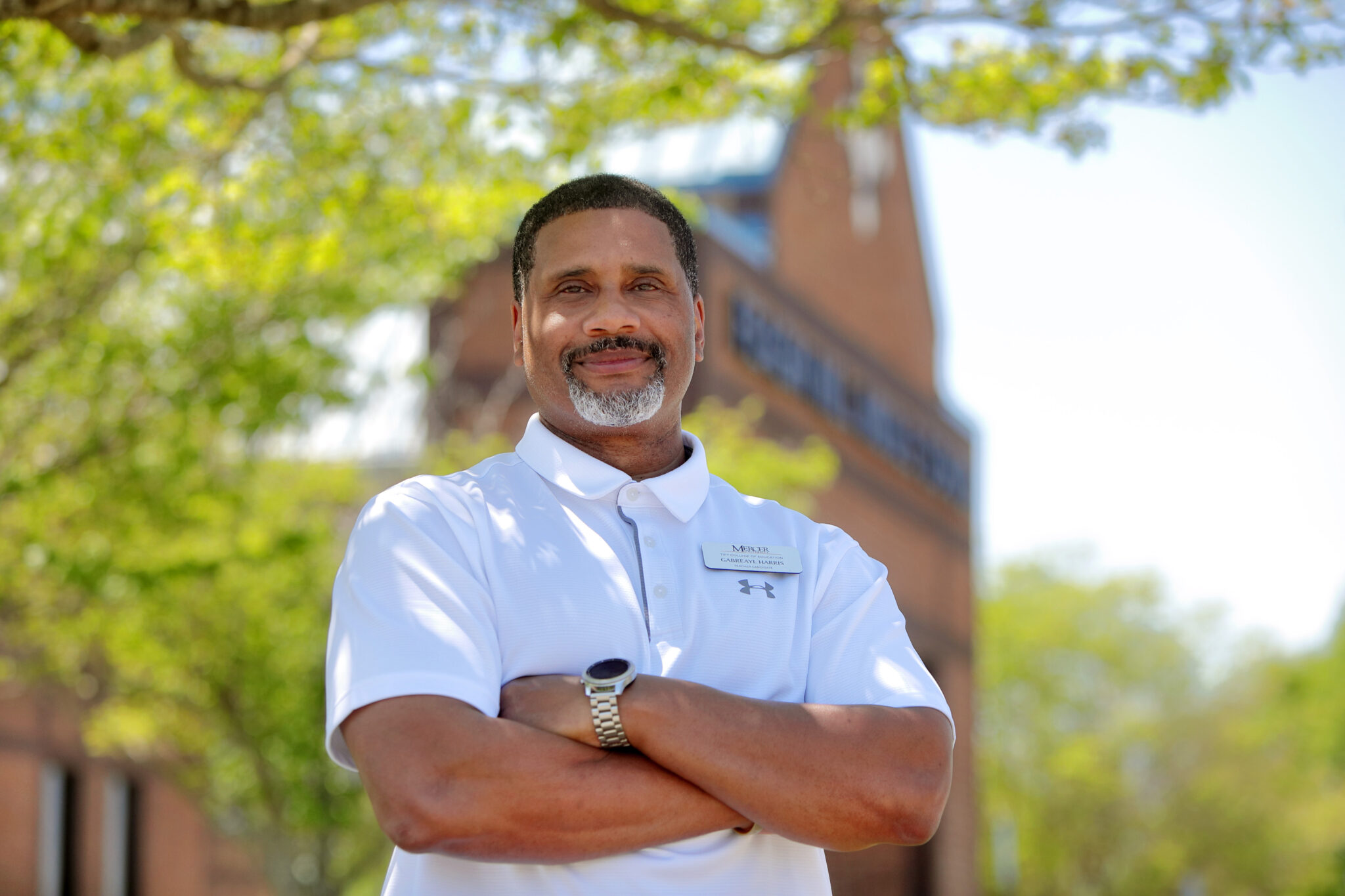 A man stands with arms crossed in front of a brick building.