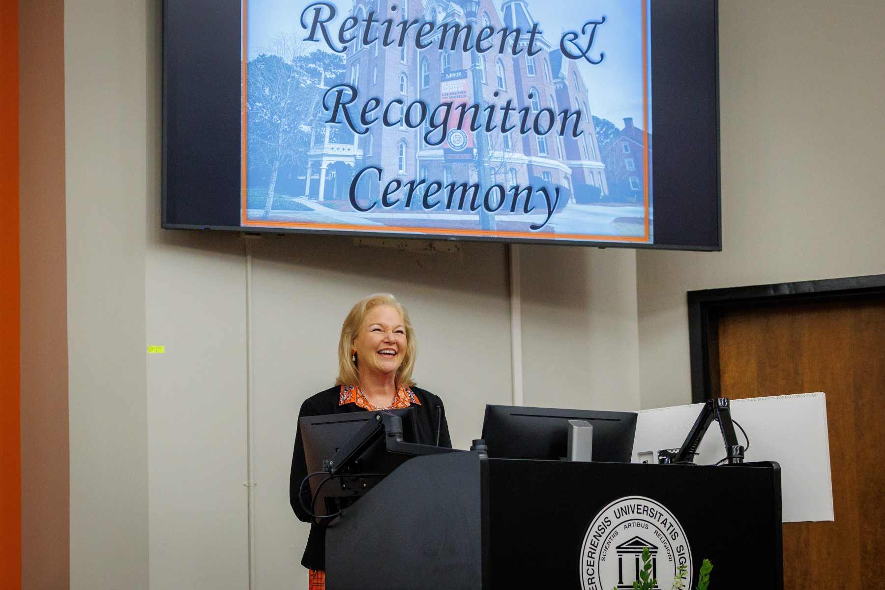 Mercer University President Penny L. Elkins, Ph.D. stands behind a podium. A sign behind her says: Retirement and Recognition Ceremony.