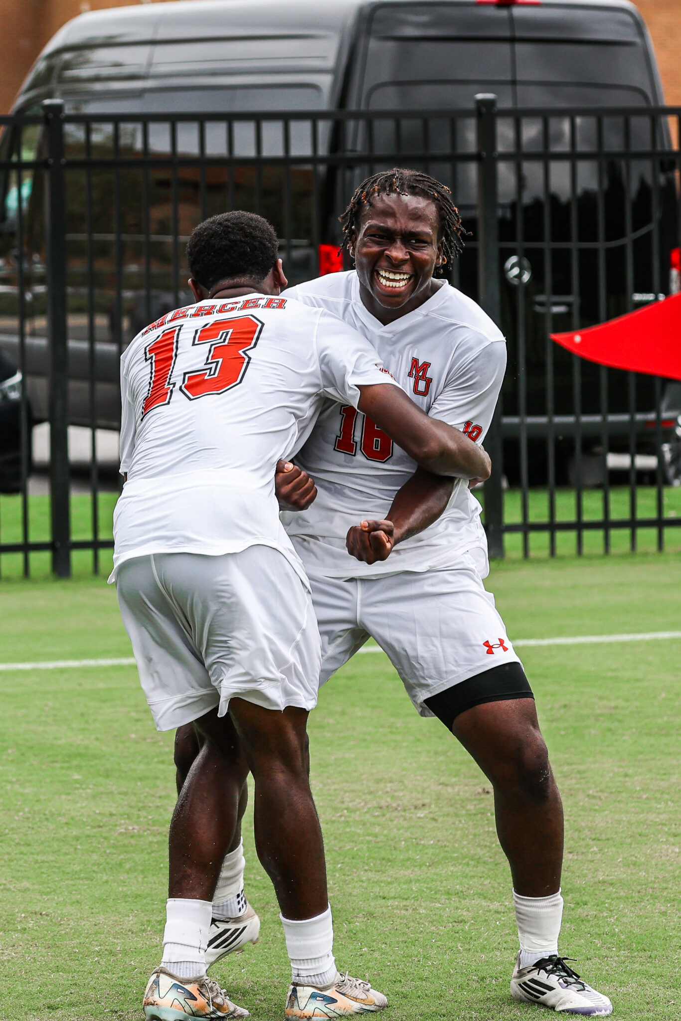 Two Mercer University men's soccer players embrace and celebrate joyfully on the field.