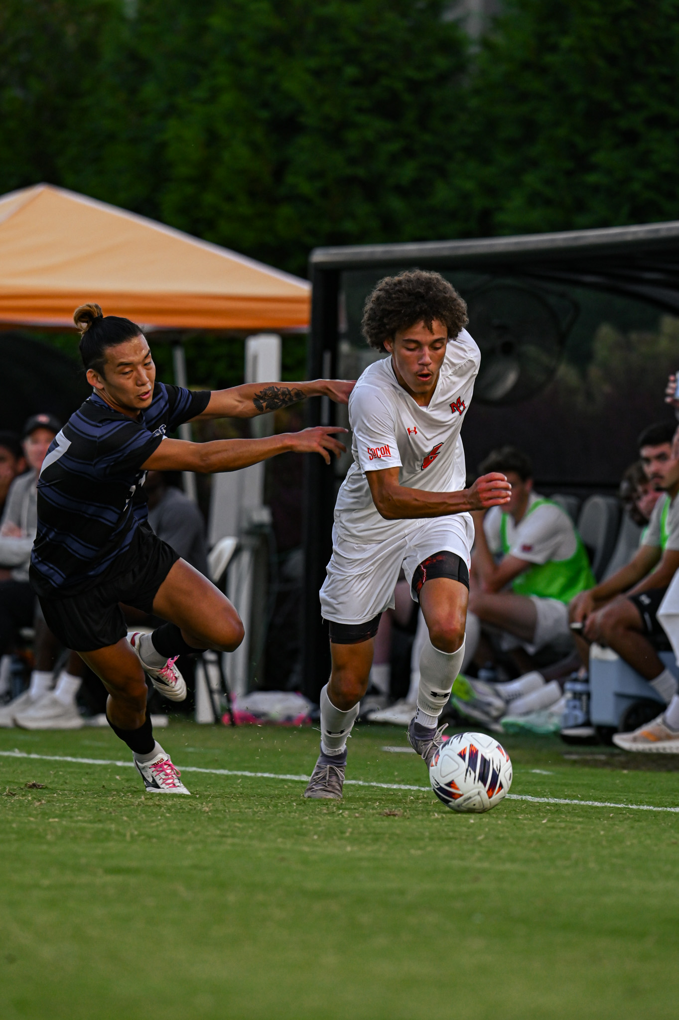 A Mercer men's soccer player dribbles the ball past a defending opponent on the field.