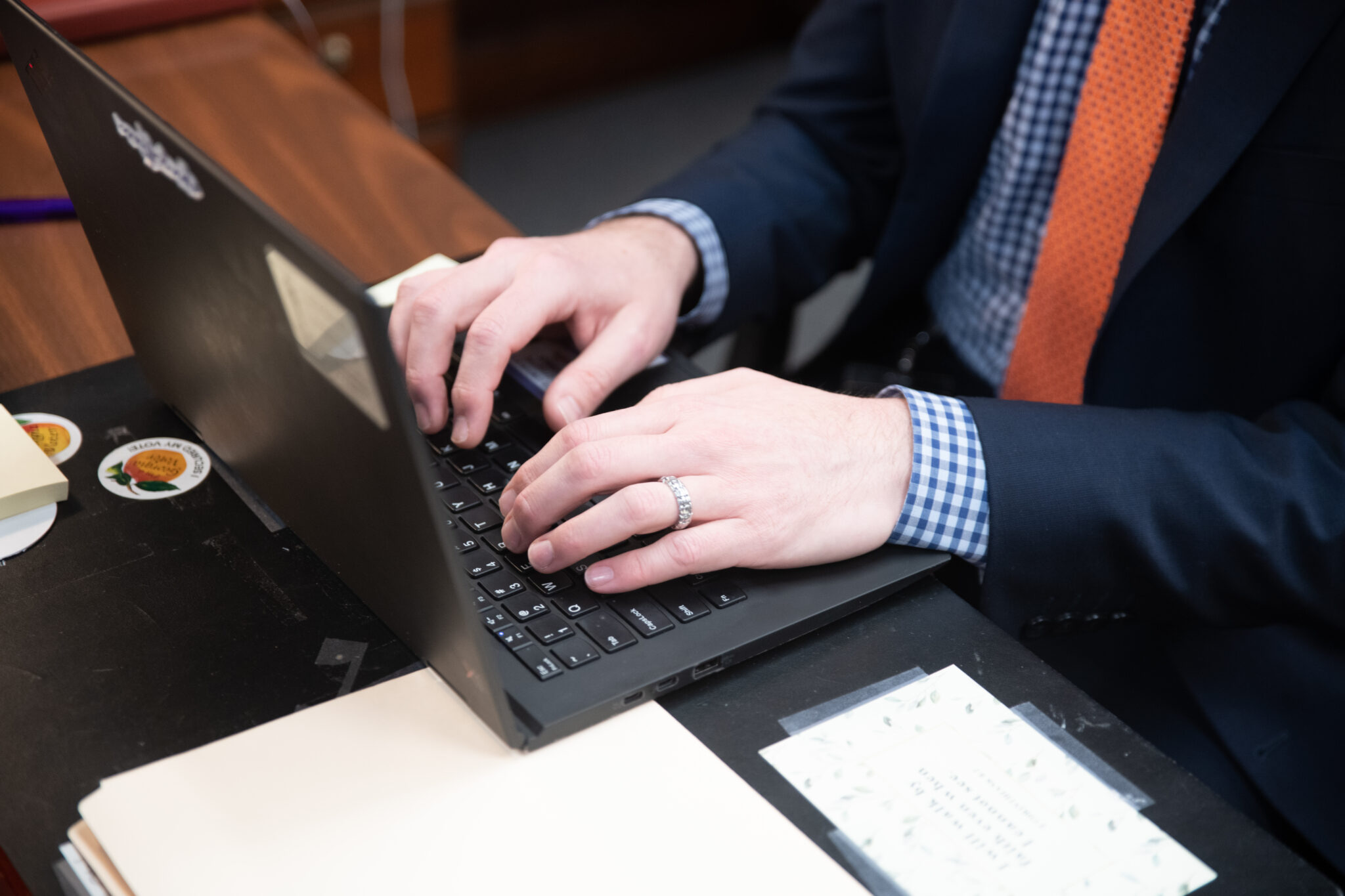 Close-up of hands typing on a black laptop at a desk.