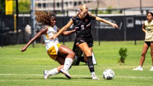 A Mercer women's soccer player battles for the ball against a sliding defender.