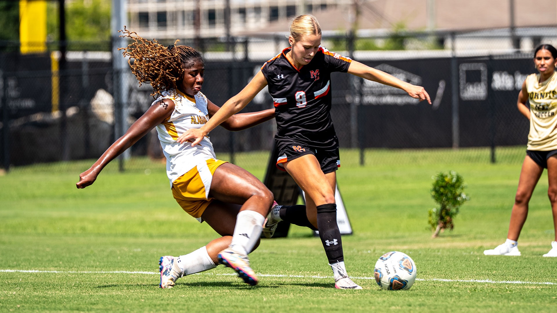 A Mercer women's soccer player battles for the ball against a sliding defender.