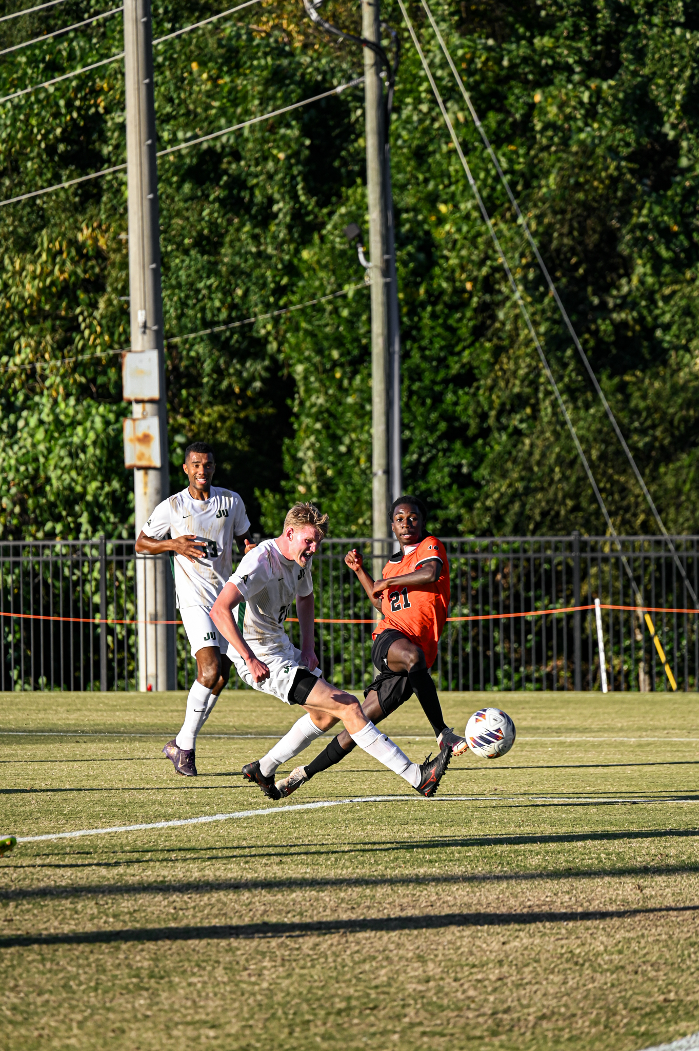 A Mercer men's soccer player battles for the ball against two opponents during a sunny match.