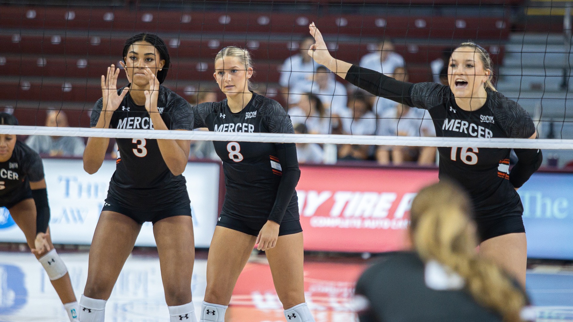 Three Mercer volleyball players line up at the net ready to block during a match.