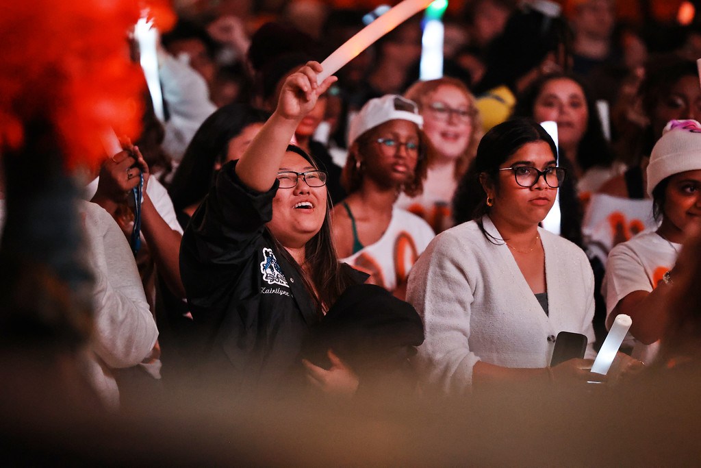 A crowd of students cheer and wave glow sticks at a Mercer University homecoming event, with orange and white colors throughout.