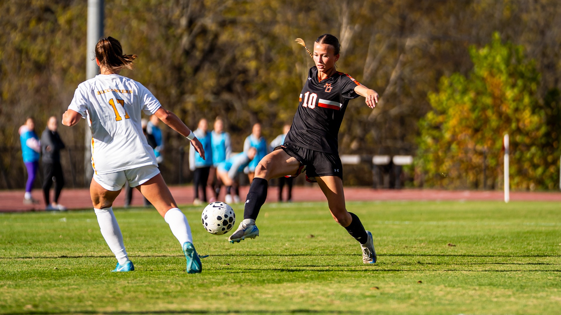 A Mercer women's soccer player kicks the ball mid-air while an opponent defends on the field.