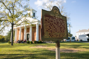A Georgia historical marker for "Old Mercer" stands in front of a white-columned brick chapel in Penfield, where Mercer University was founded in 1833.