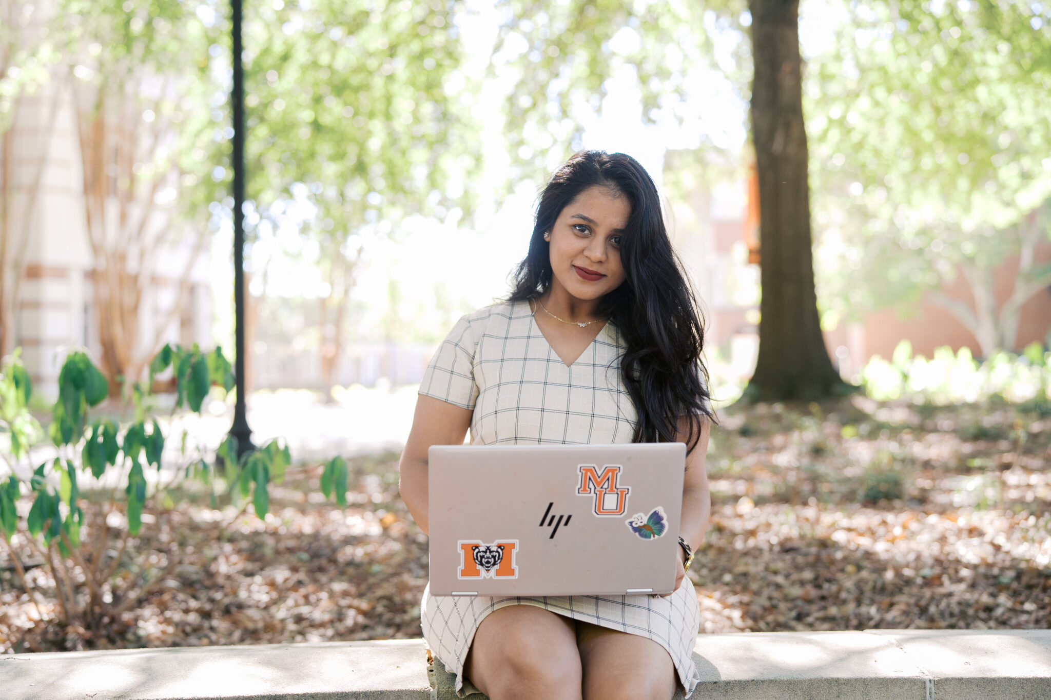 A Mercer business student sits on a ledge while balancing an open laptop on her lap.