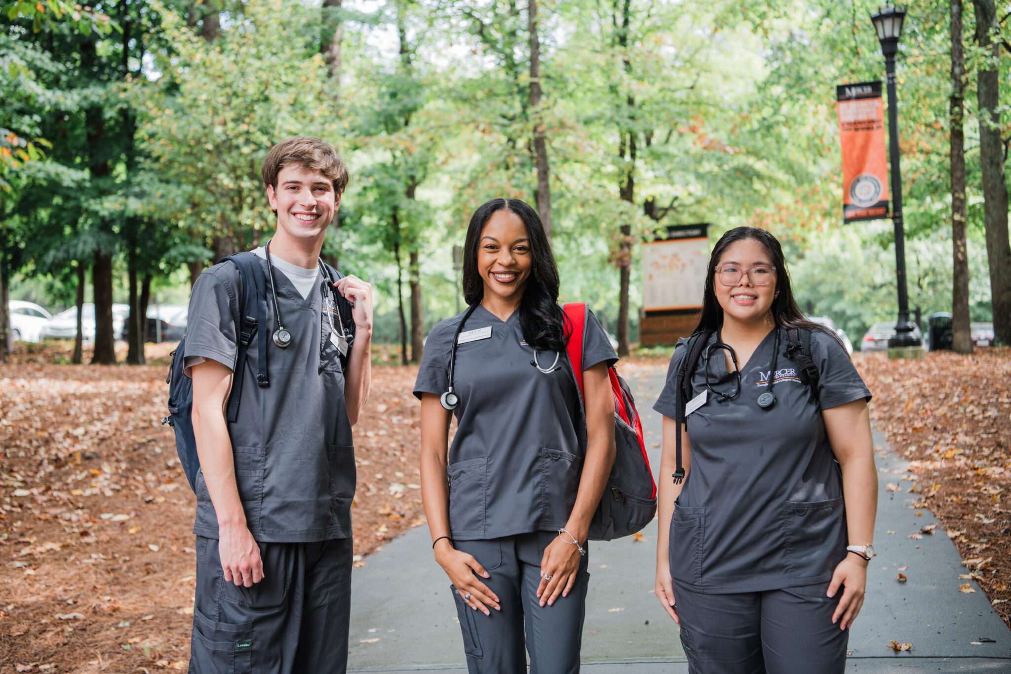 Three nursing students wearing scrubs stand on a walkway on Mercer's campus.
