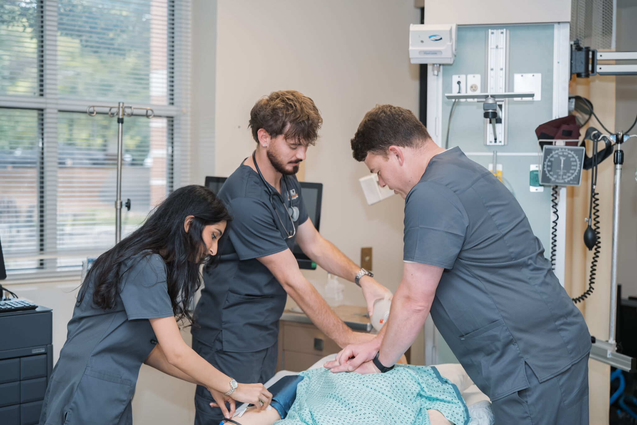 Mercer nursing students wearing scrubs work on a mannequin in a simulated hospital room.