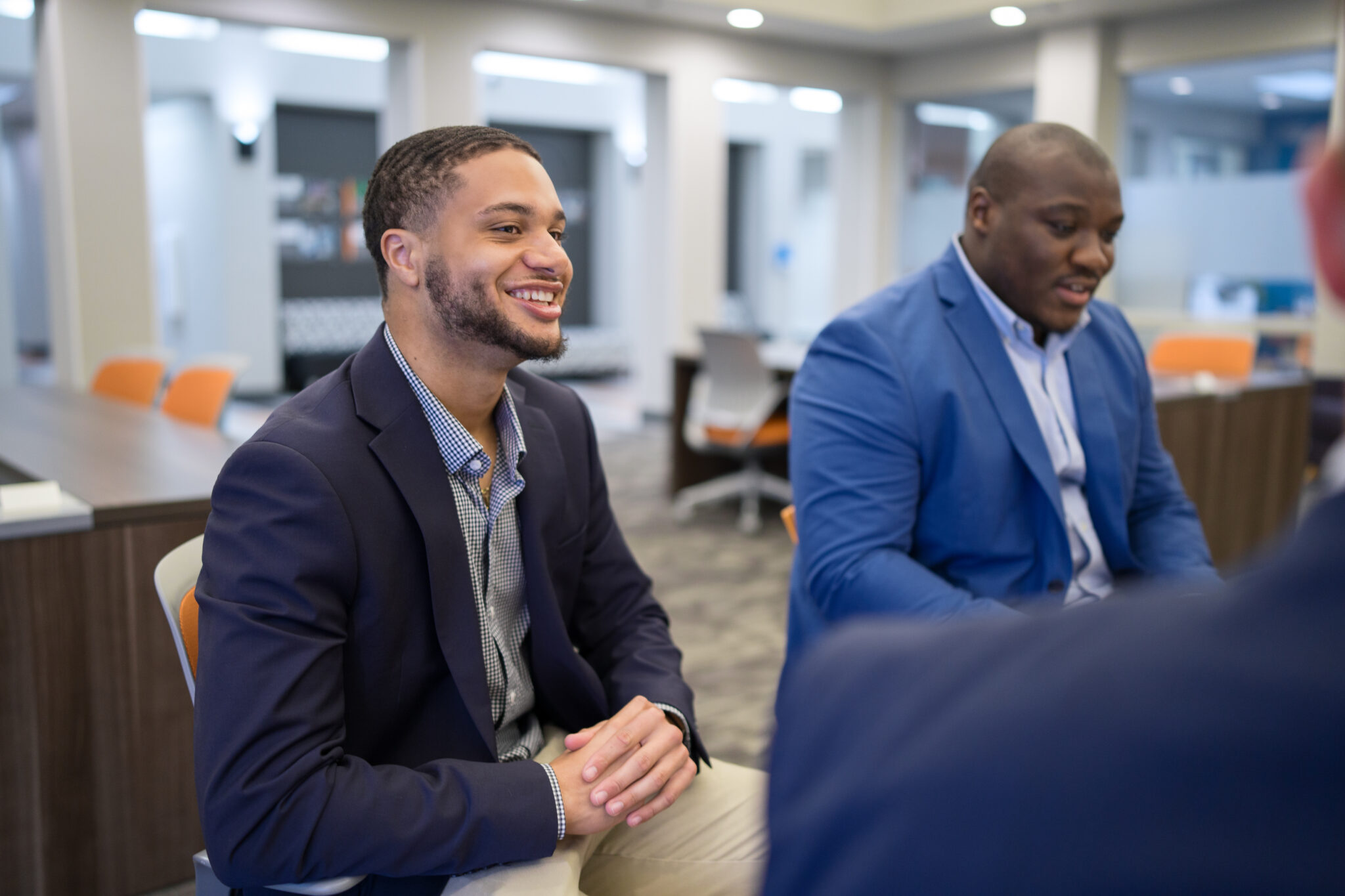 Two Mercer students in business attire sit and talk at a table in a modern office setting.