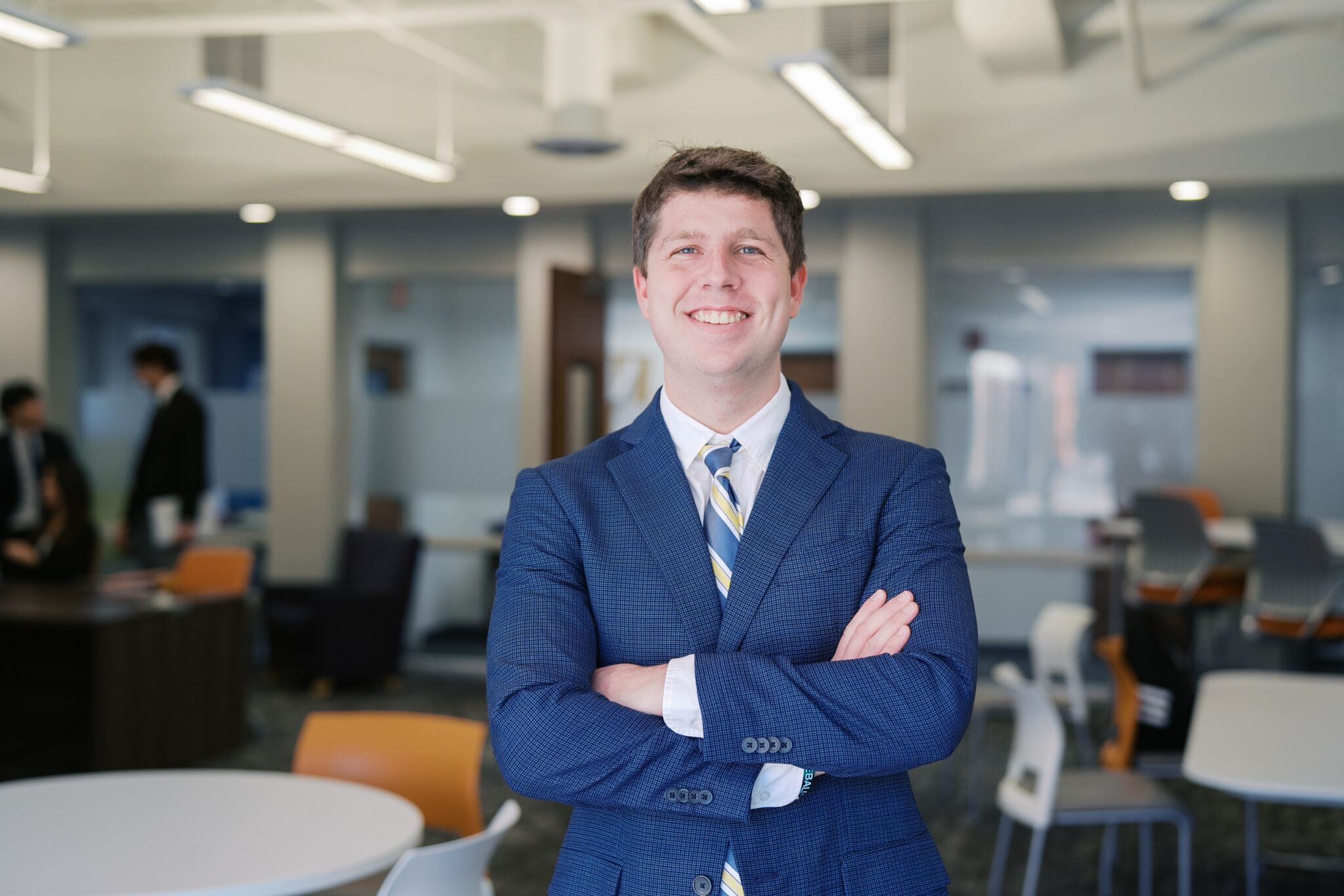 A Mercer student wearing a business suit stands smiling with his arms crossed in a classroom.