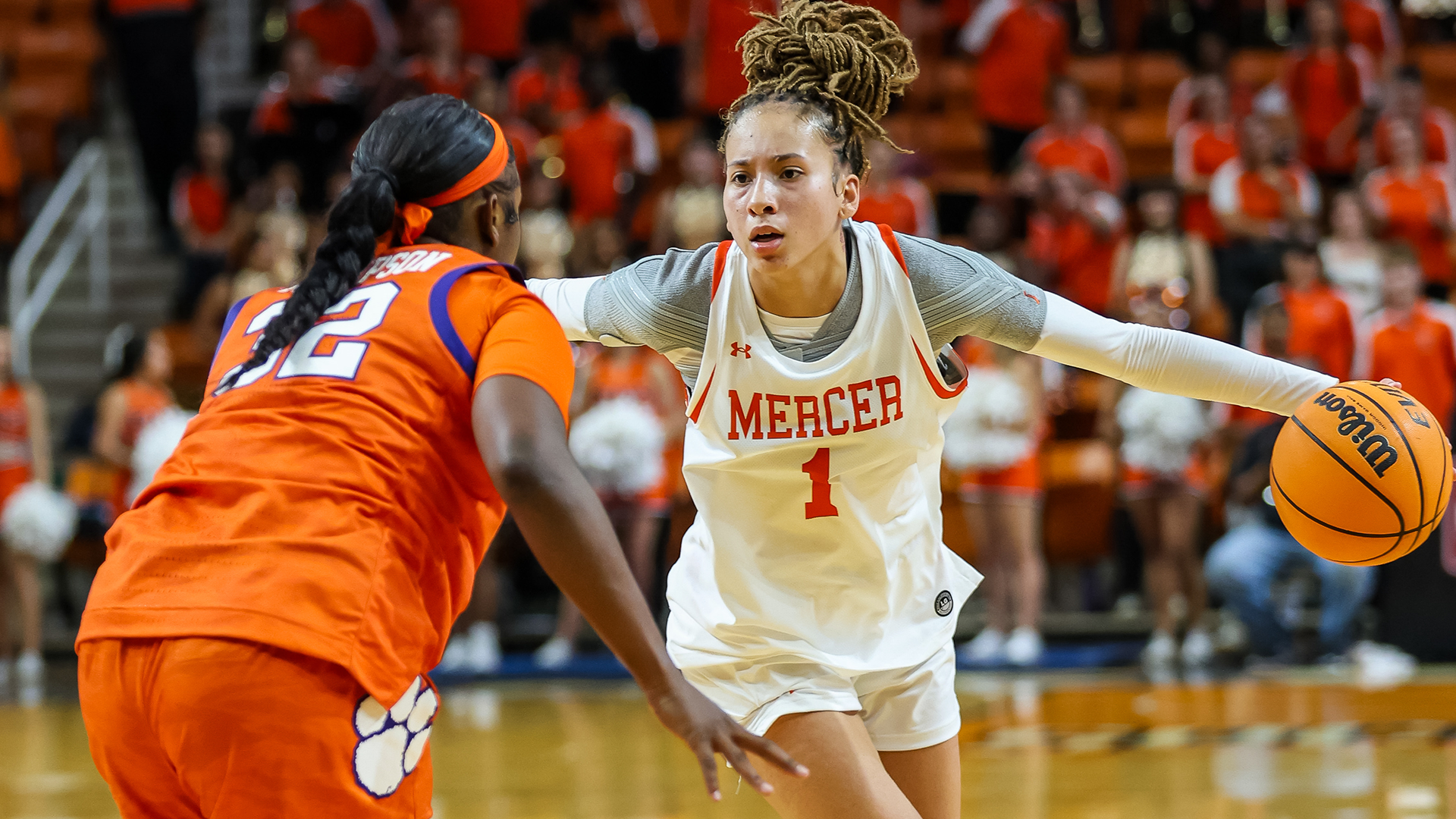 A Mercer women's basketball player dribbles the ball around a defender during a game.